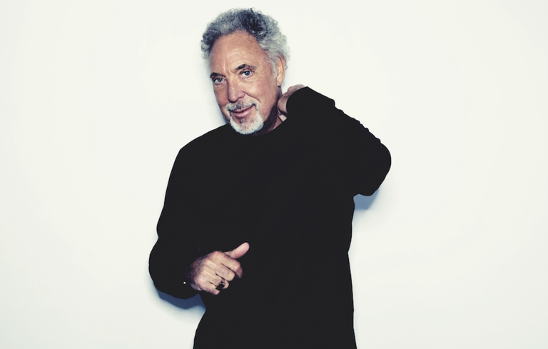 Studio portrait of Welsh singer Sir Tom Jones in a black long-sleeve sweater against a white backdrop.